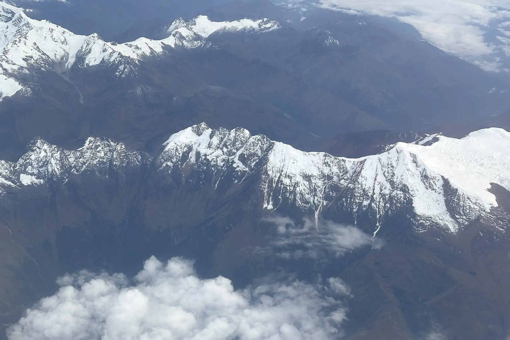 Snow-covered ridges of the Peruvian Andes seen from a plane, the range a South America itinerary has to cross