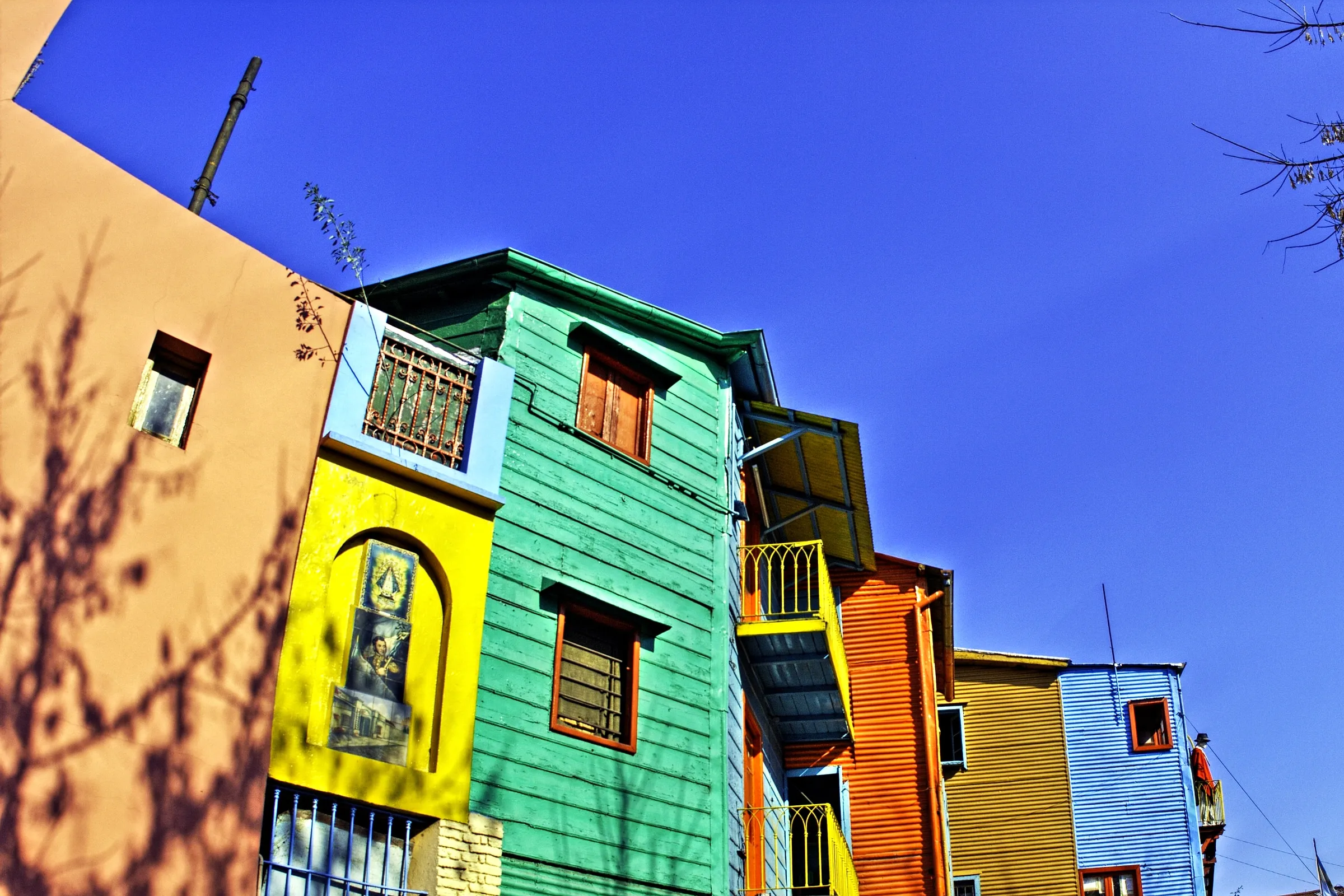 The painted wooden and corrugated-iron houses of Caminito in La Boca, in green, yellow, orange and blue under a deep blue sky