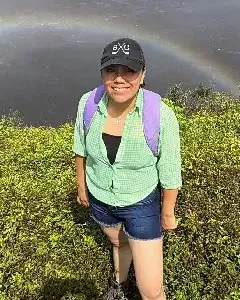 Carolina Inlago on a green hillside with a rainbow over the valley behind her