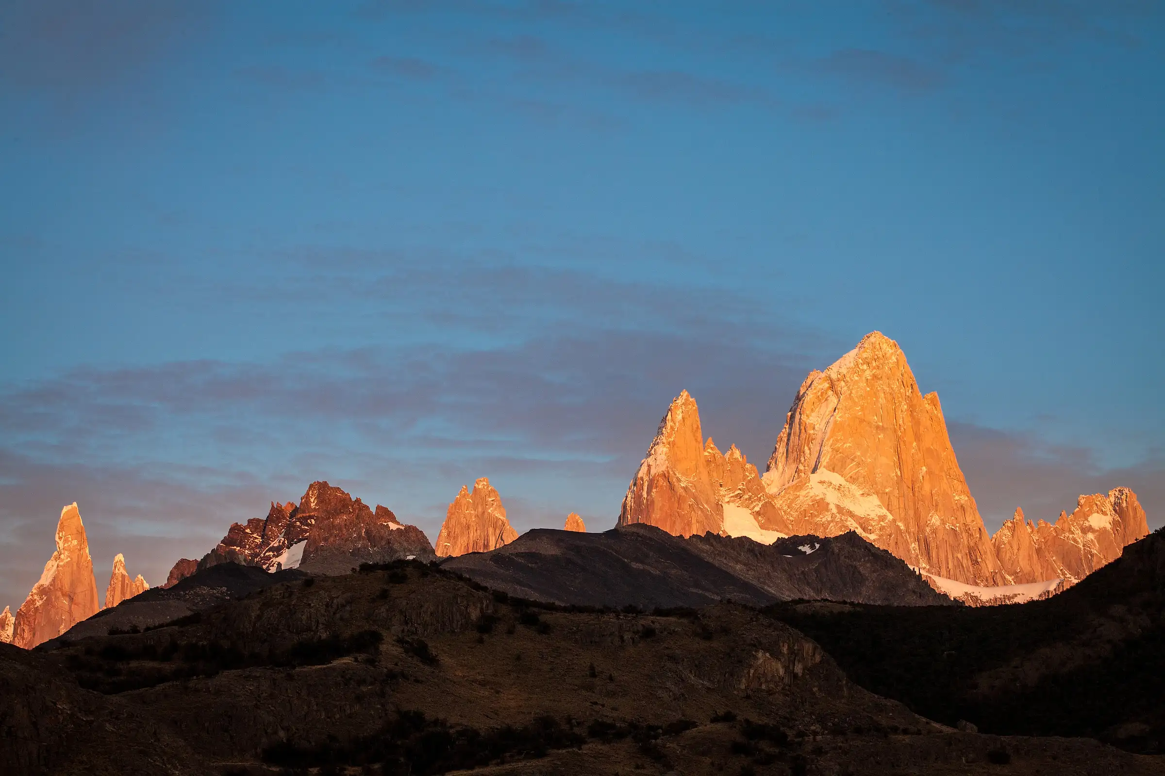 Fitz Roy and Cerro Torre lit orange at sunrise above the dark hills outside El Chaltén, Argentine Patagonia