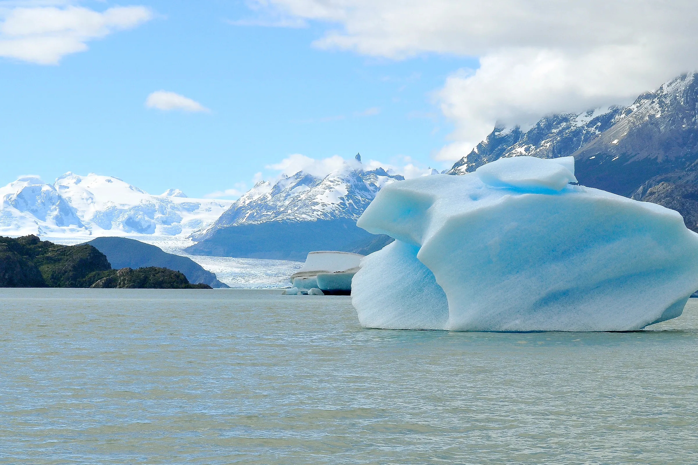 A blue iceberg floating on Lago Grey with the Grey glacier and snow-covered mountains behind, Torres del Paine, Chile