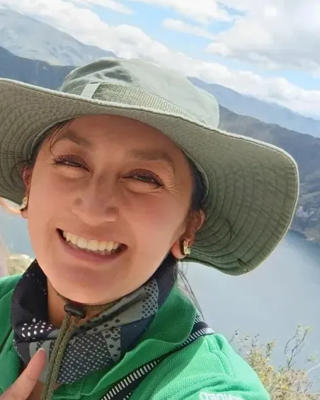 Irene Minda in a wide-brimmed hat, smiling above a crater lake