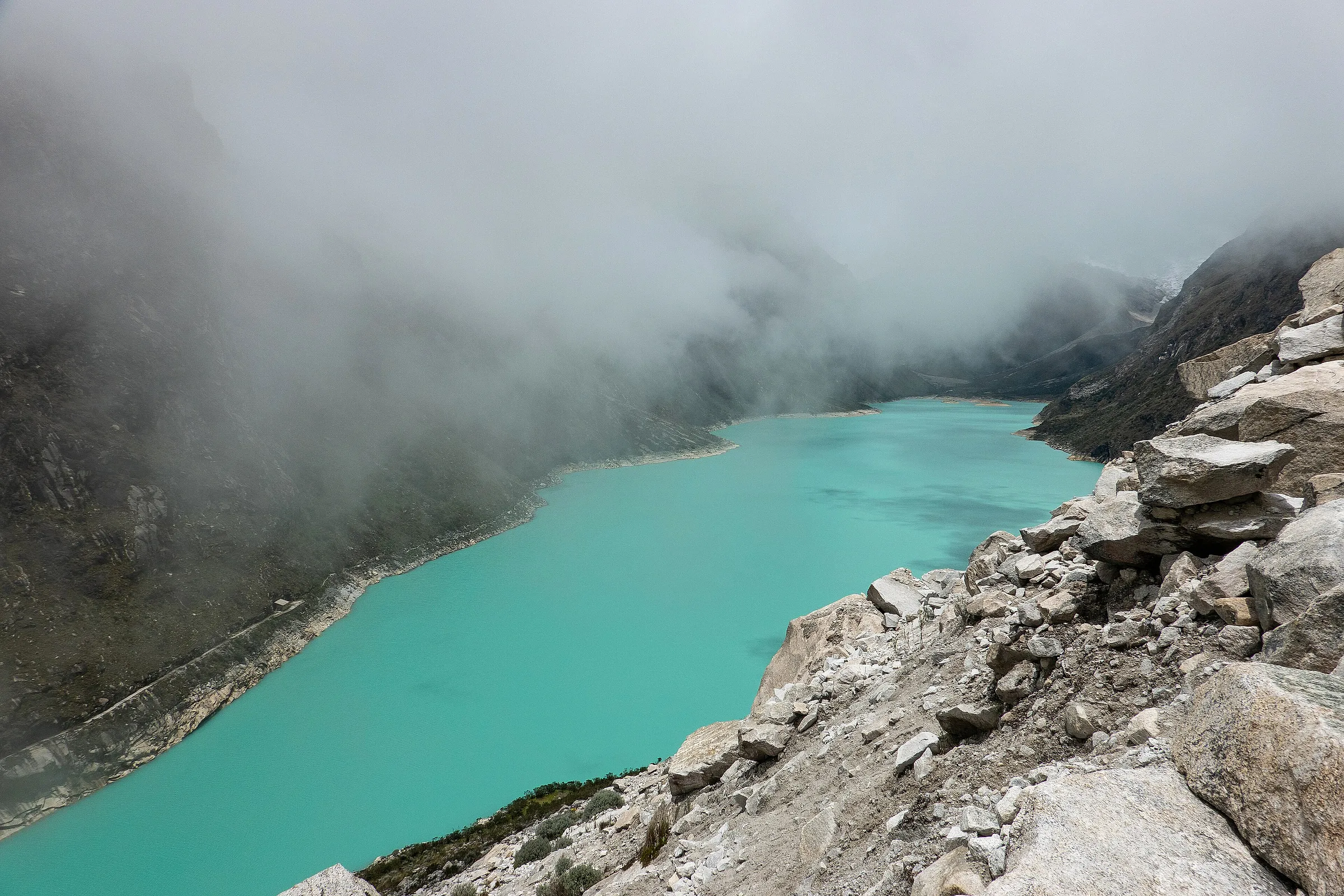 Turquoise Laguna Parón under cloud, with the rock walls of the Cordillera Blanca rising from its shore