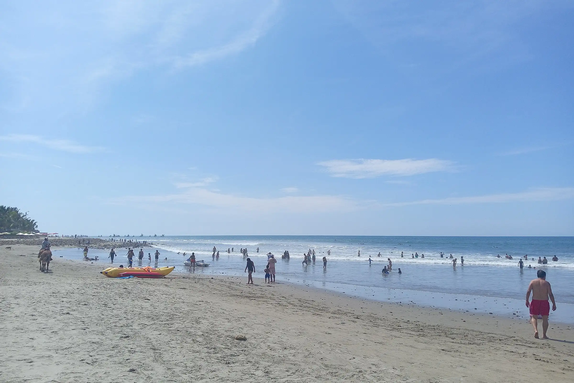 Swimmers in the surf on the long sandy beach of Máncora under a clear sky, northern Peru