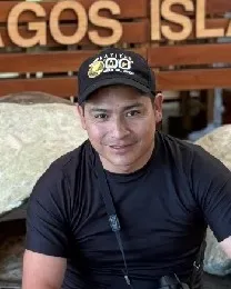 Pedro Toaquiza sitting in front of the Galápagos Islands sign with a camera