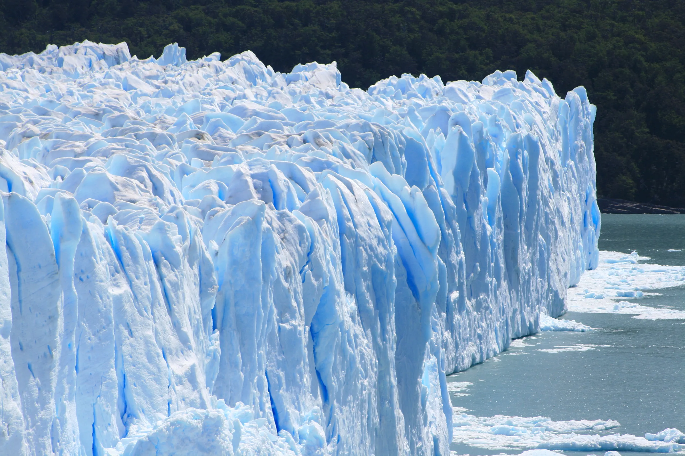The blue face of the Perito Moreno glacier above the grey water of Lago Argentino, close up from the walkways