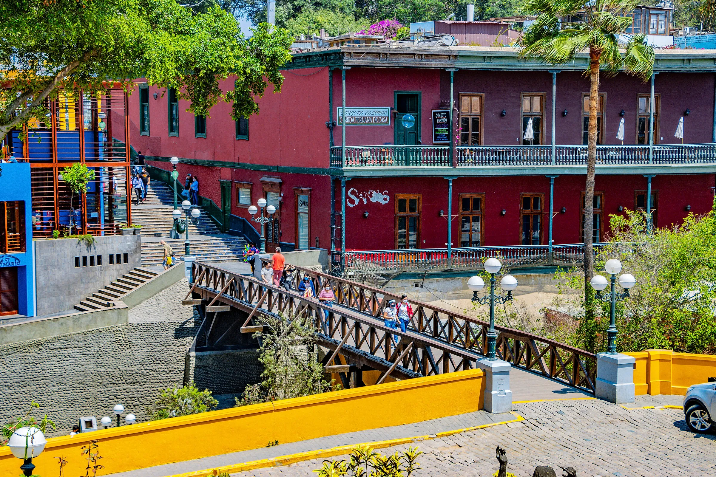 The wooden Puente de los Suspiros crossing the Bajada de Baños beside a red mansion in Barranco