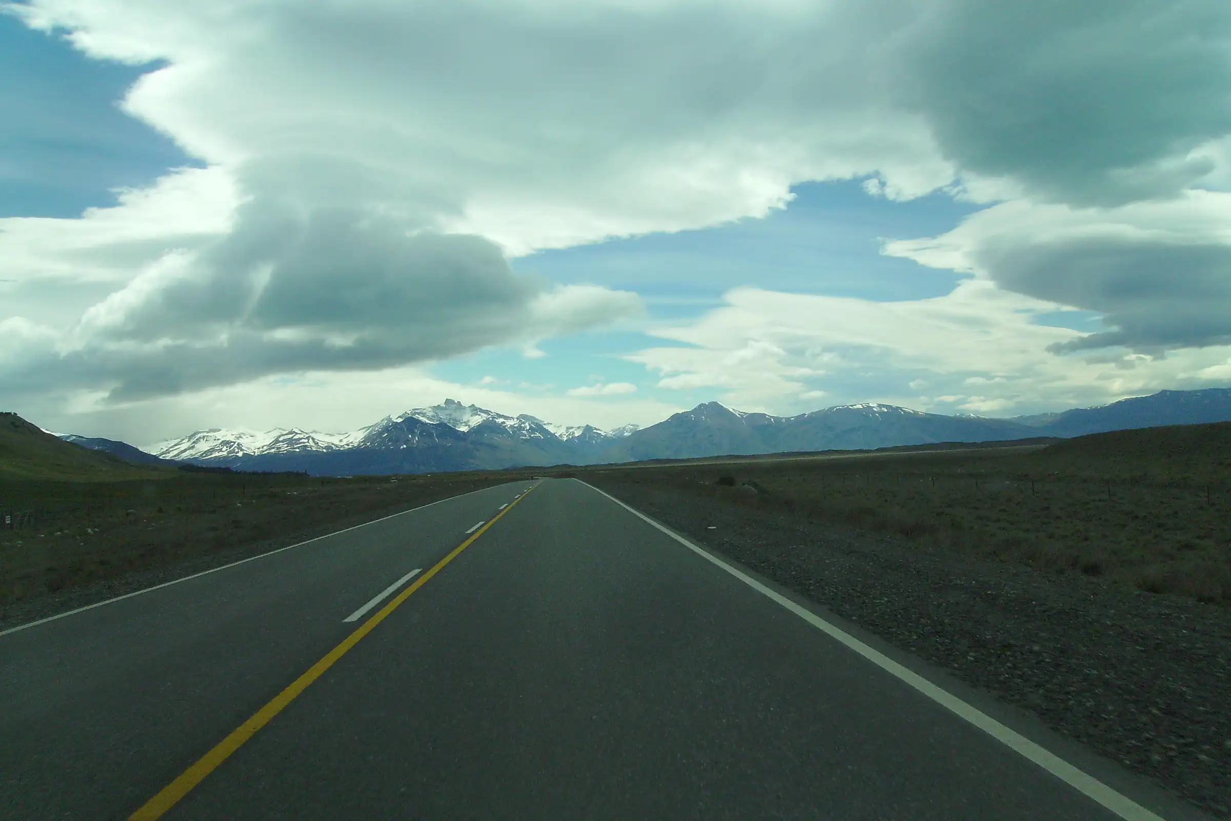 An empty paved road crossing the Patagonian steppe towards snow-capped Andes under heavy clouds, Santa Cruz, Argentina